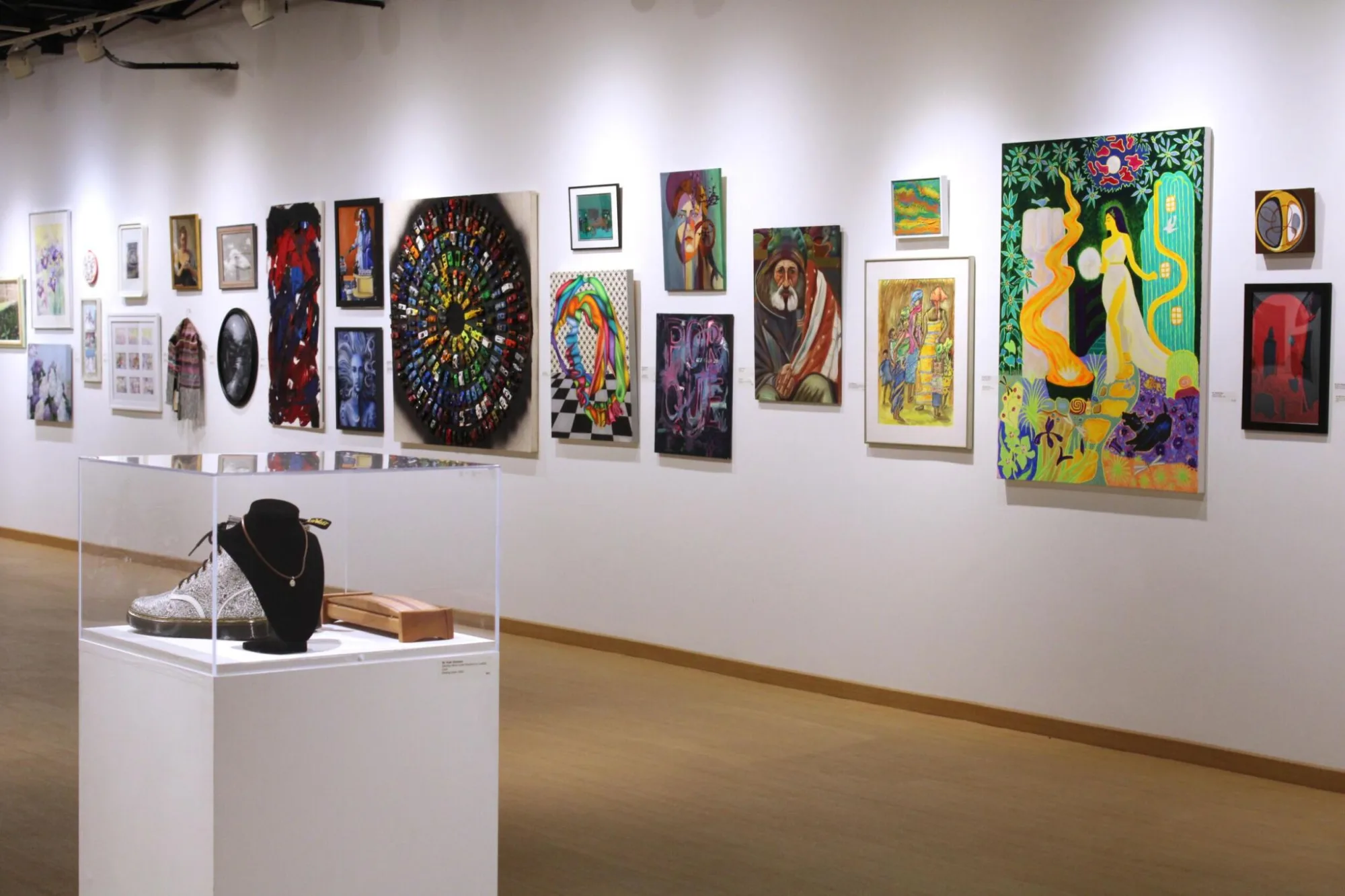 A gallery with various colorful paintings on the wall and a display case containing jewelry.