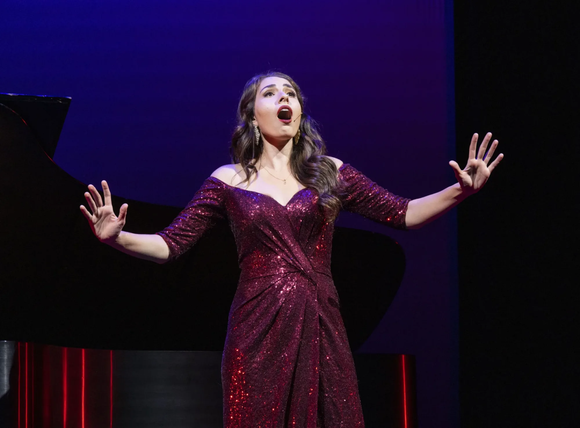 Woman in purple gown sings on stage with her arms open wide.