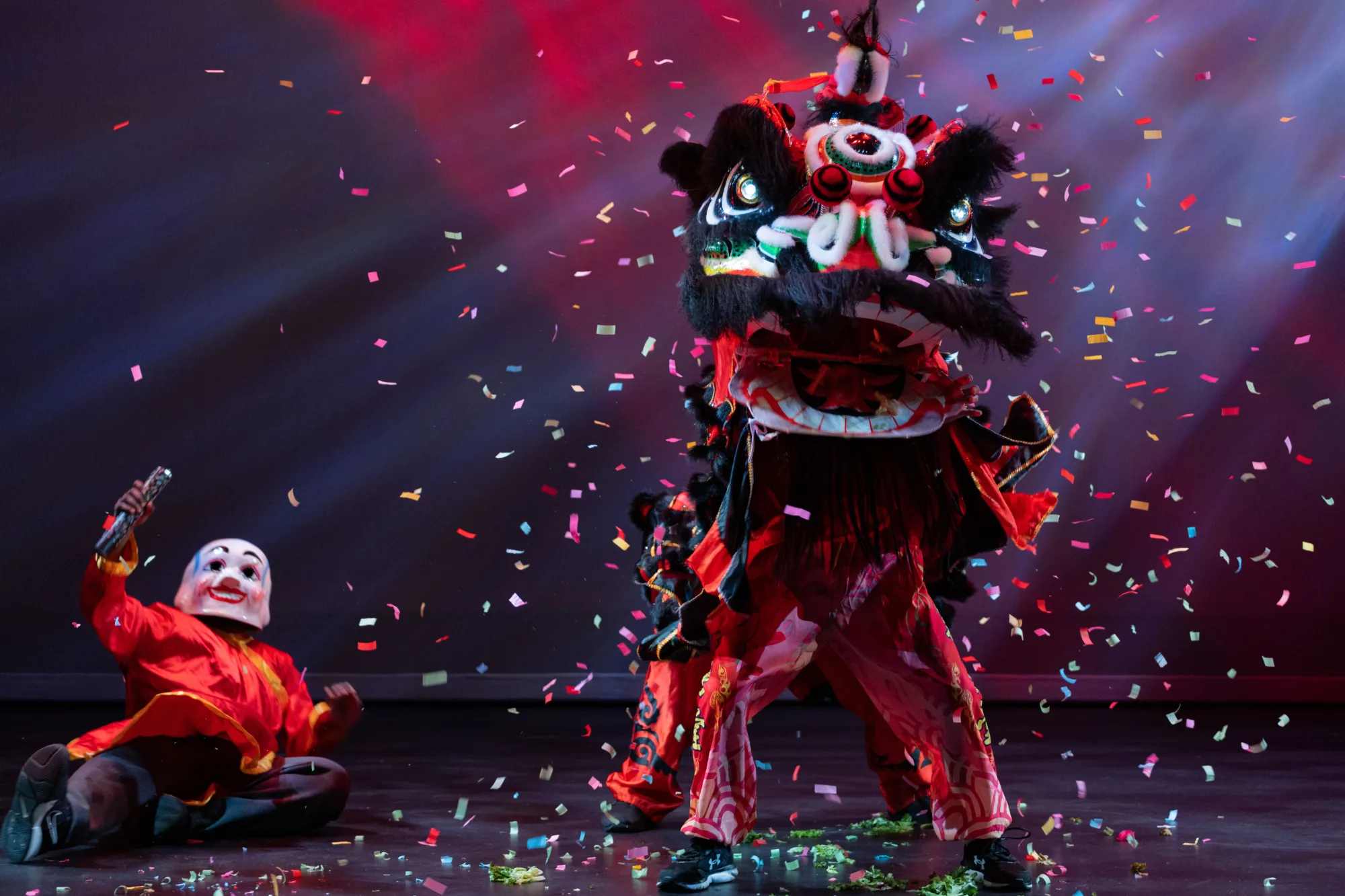 Two dancers wearing a large lion head and one dancer wearing a mask surrounded by confetti