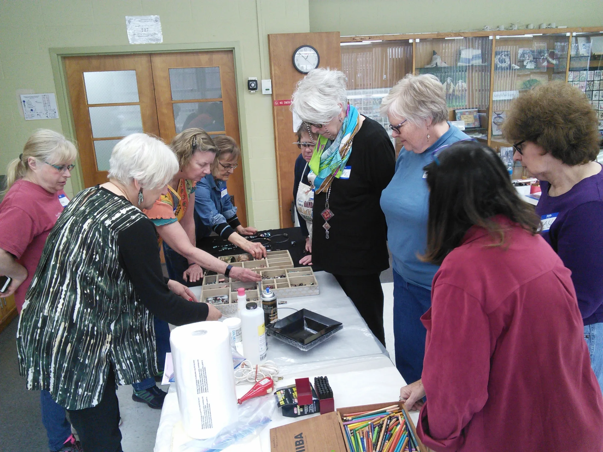 A group of ladies gathered around a table with beads and crafts on it