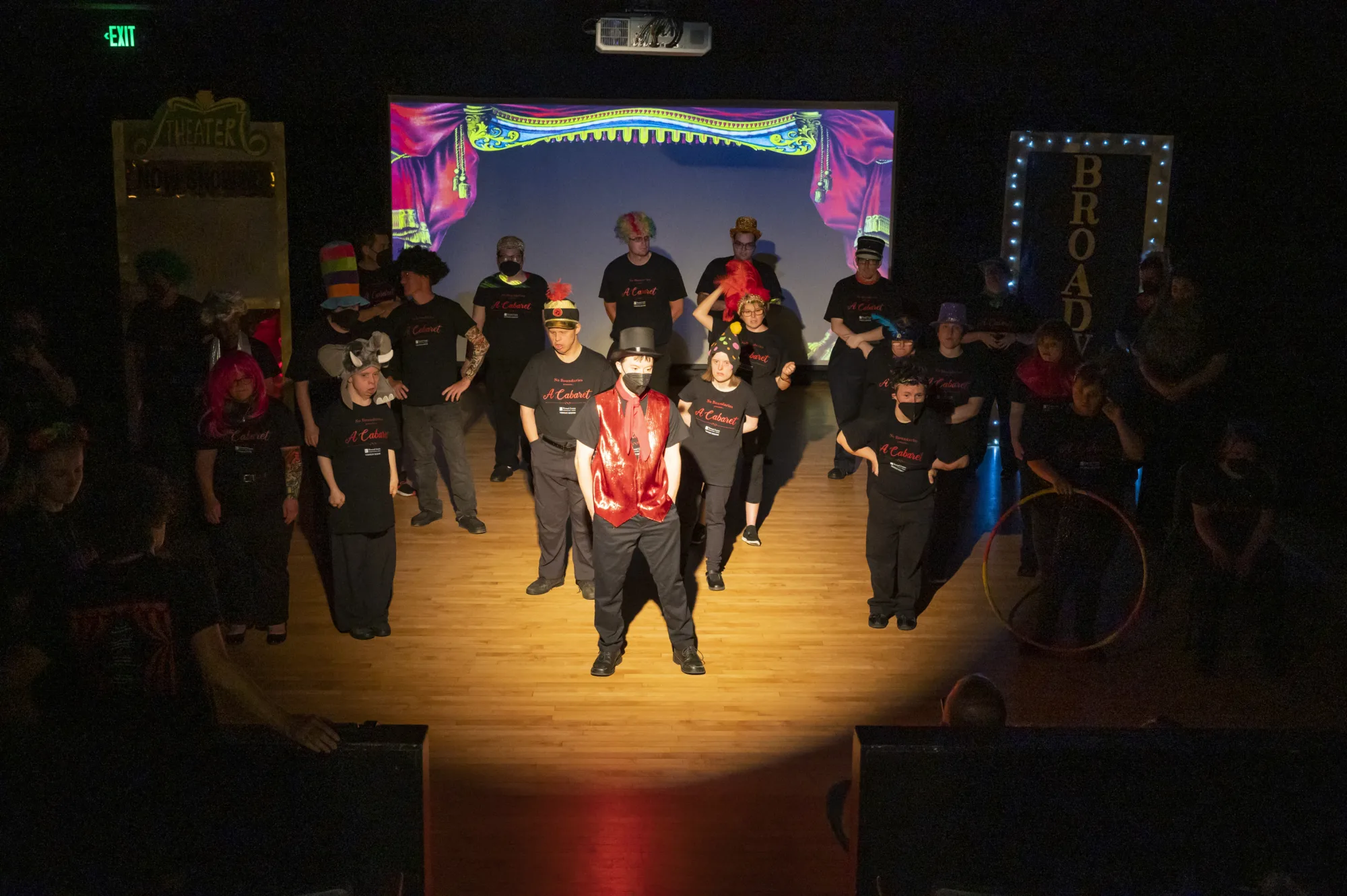 Group of actors standing on stage in costume with theatre lights