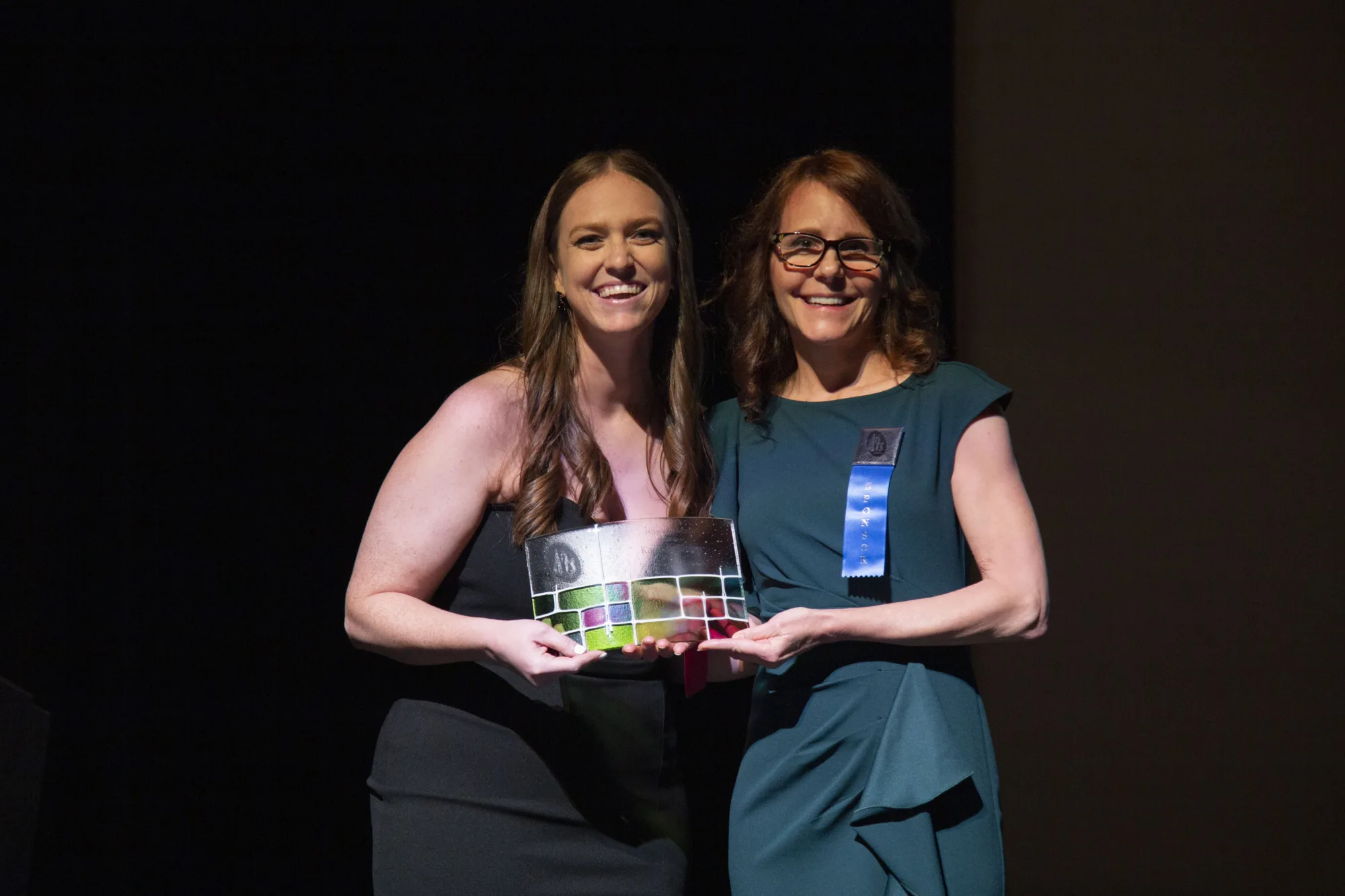 Two smiling women hold glass award.