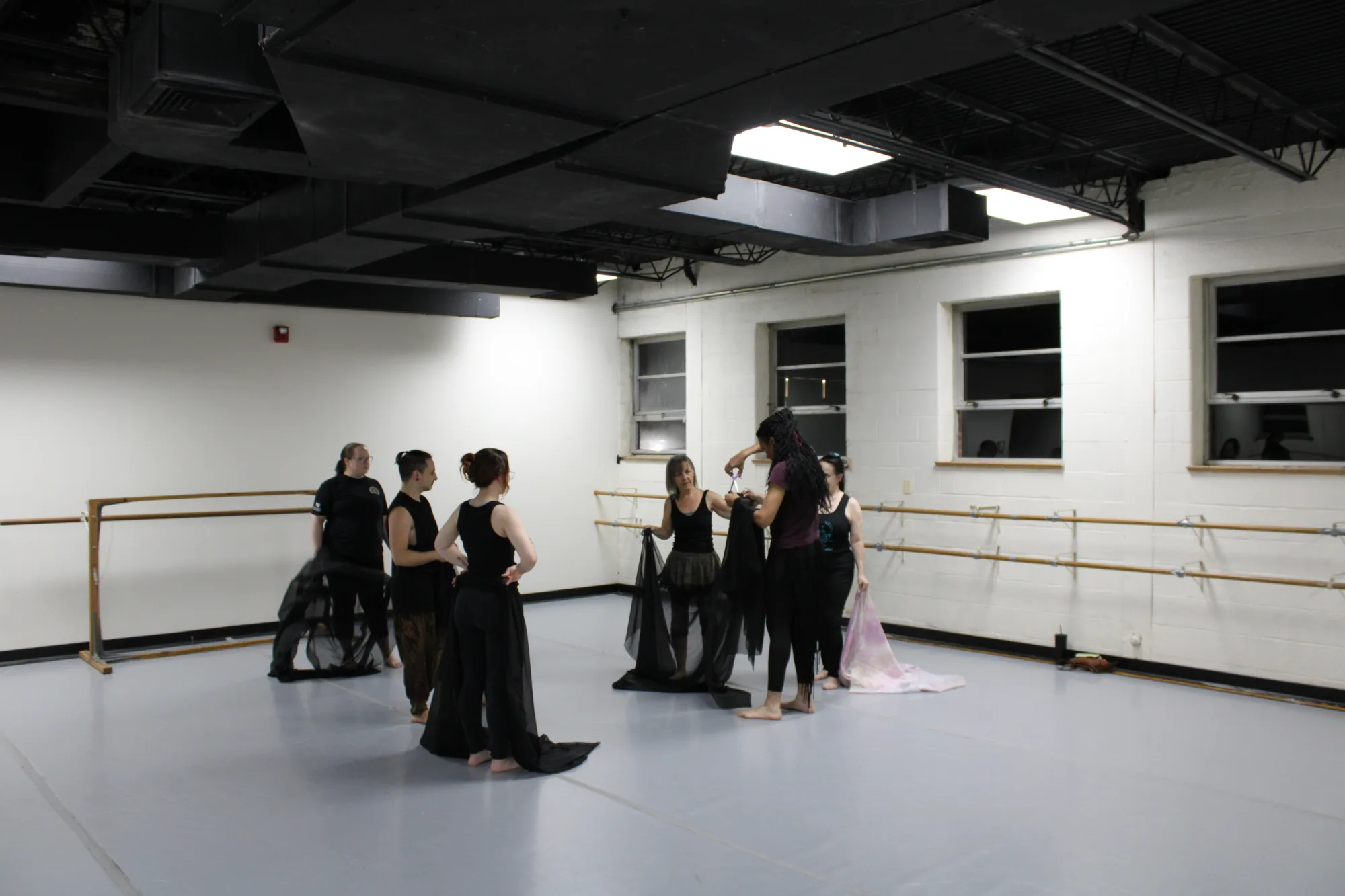 Dancers stand together in a group fixing a scarf with dark windows behind them
