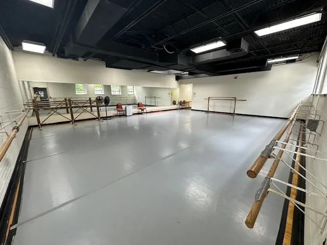 Empty dance studio with mirrors on one wall, windows on the opposite side, and ballet barres throughout