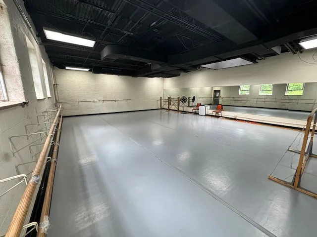 Empty dance studio with mirrors on one wall, windows on the opposite side, and ballet barres throughout
