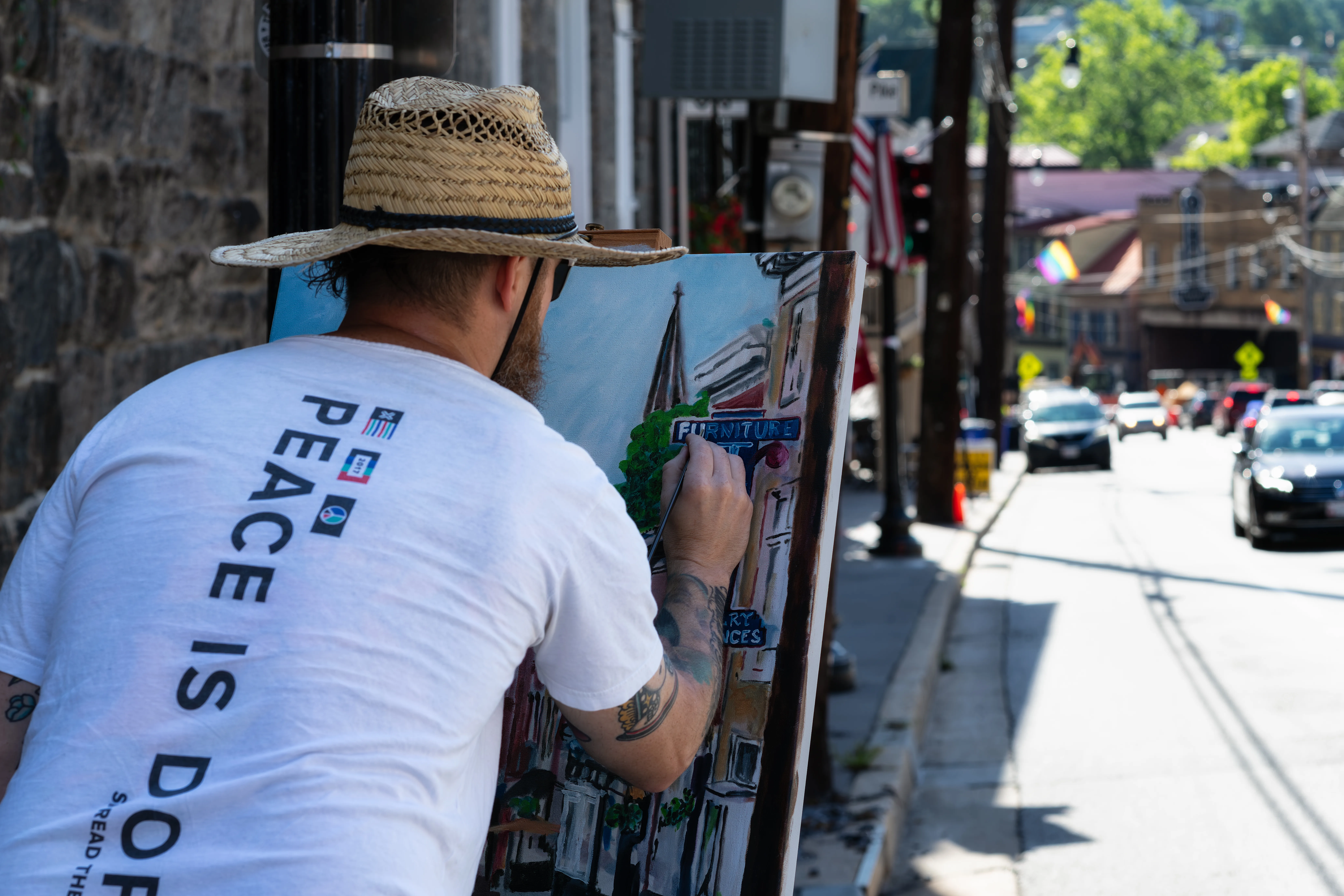 Man wearing straw hat paints downtown scene outdoors.