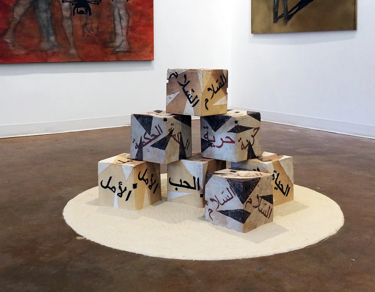Sand in a circle on the floor with cubes stacked in pyramid style, one cube in front on top of it.