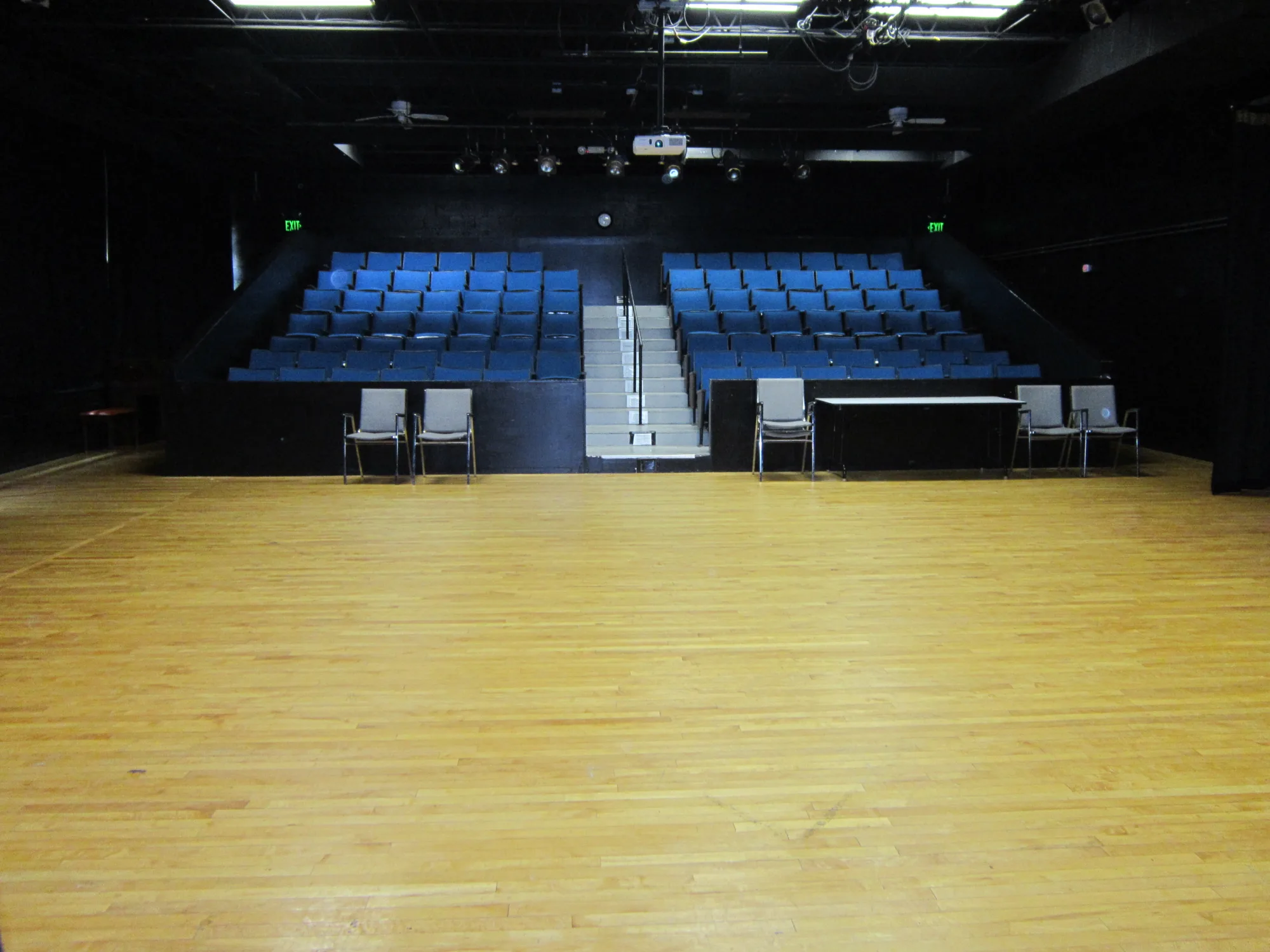 Empty black box theatre with blue seats and hardwood flooring