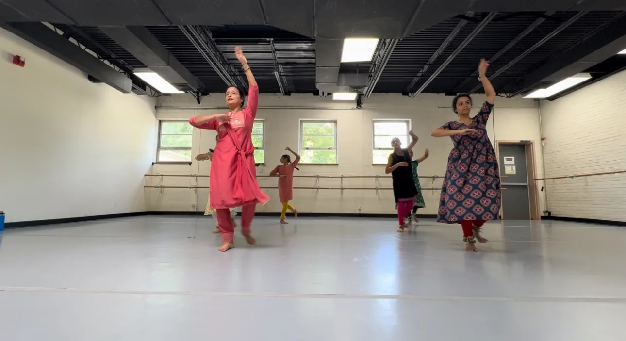 Six women in Indian dresses actively dancing with windows behind them