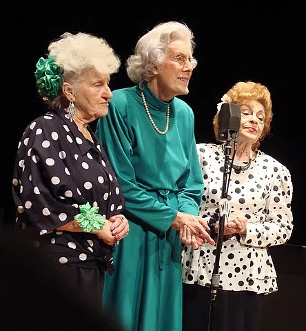 Three women standing on a dark stage in front of a microphone