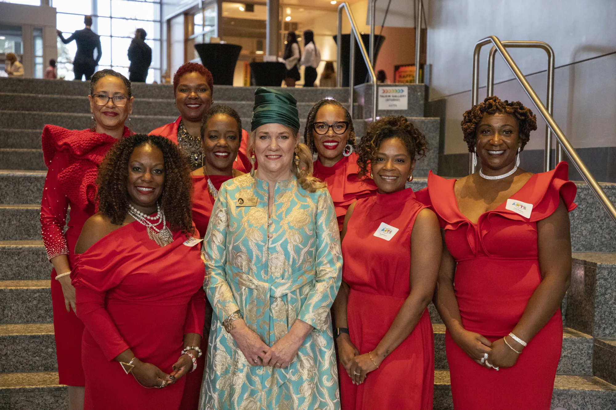 A group of women in red pose on staircase with one woman in blue in center.