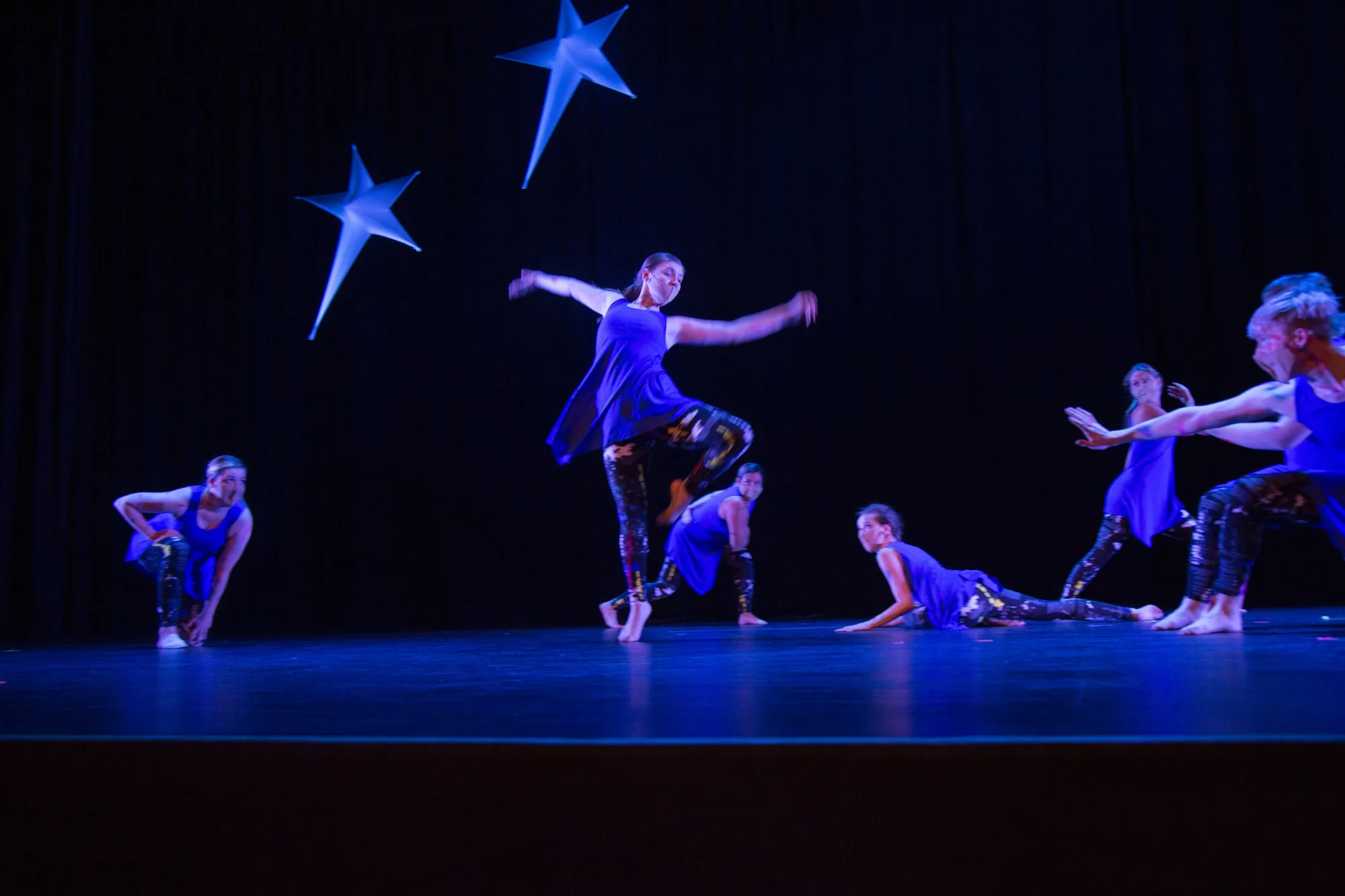 Dancers in blue costumes perform on stage under star-shaped decorations.