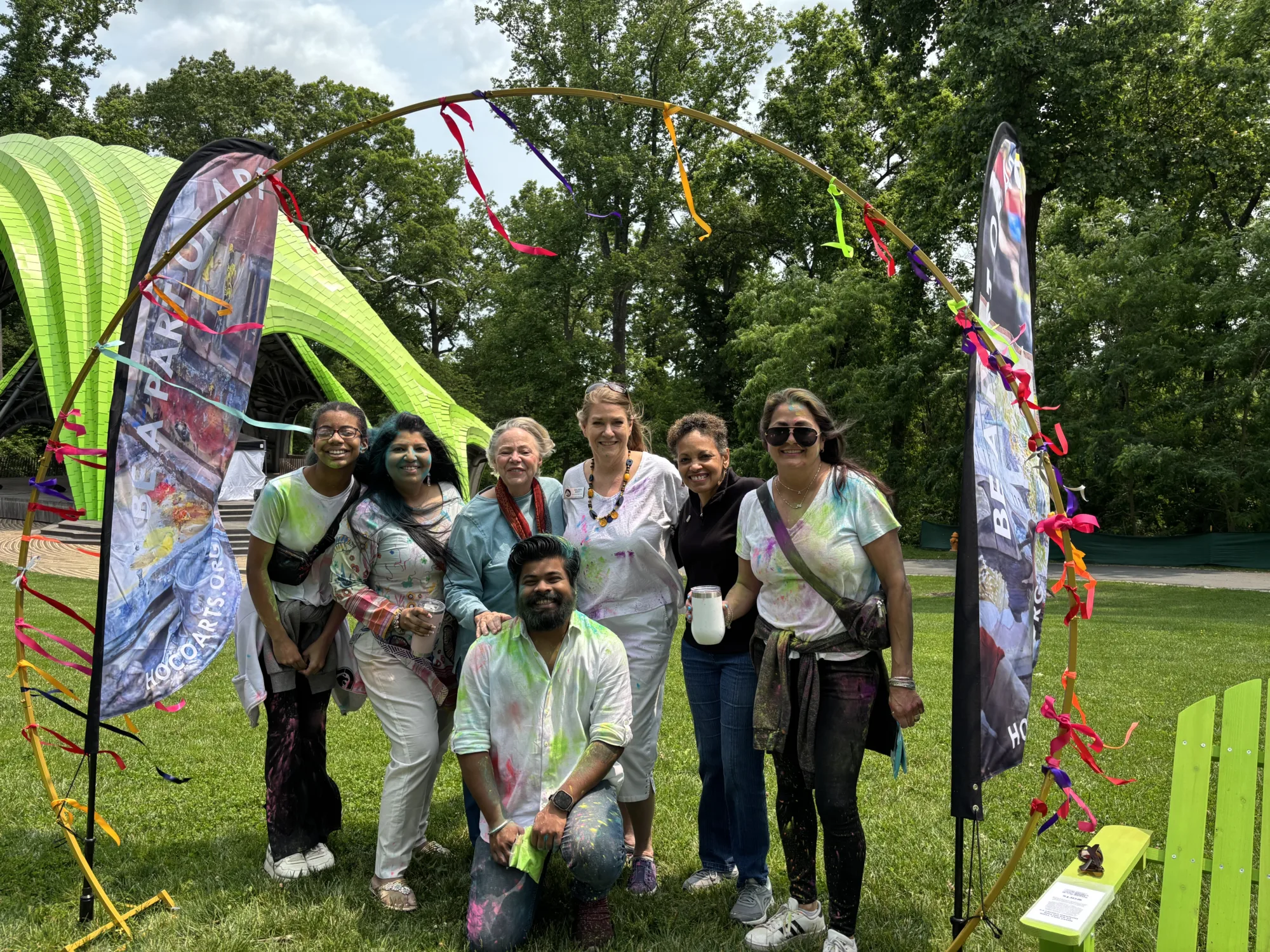 A group of people covered in colorful powder standing inside a hoop tied with colorful ribbons.