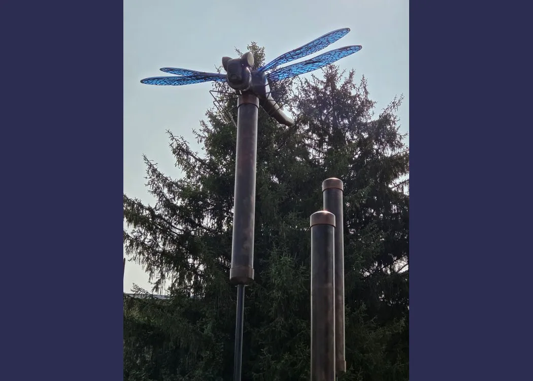 a high sculpture of a dragonfly made from recycled materials with blue glass wings