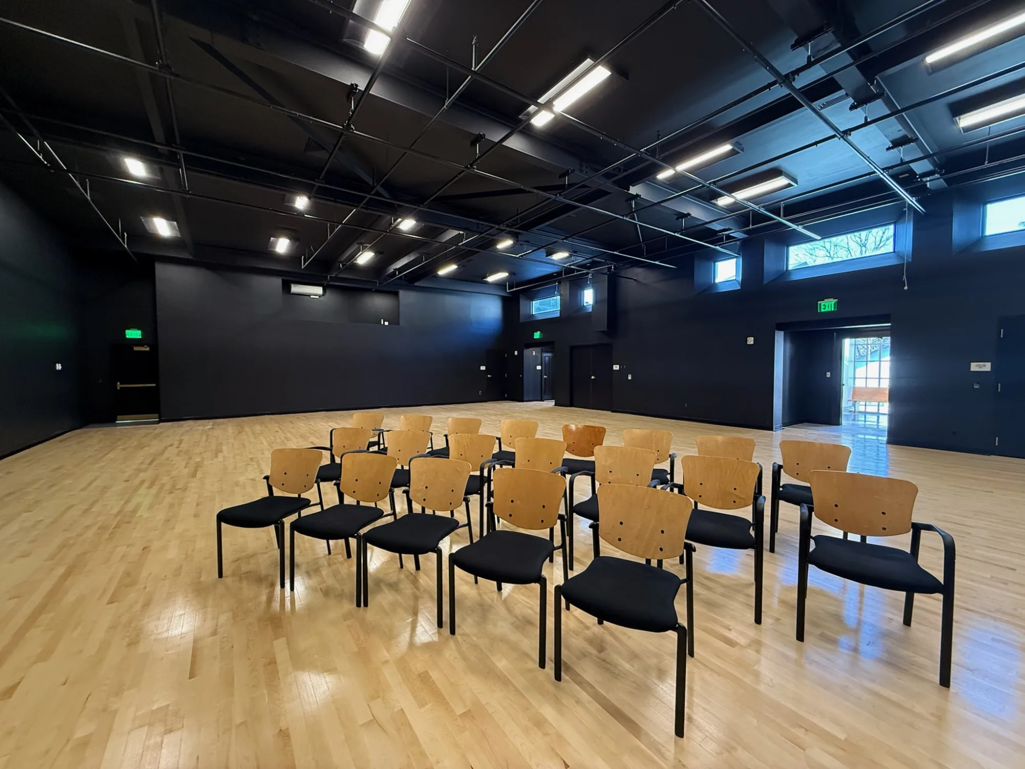 large room with black walls and a wooden floor with chairs in the foreground